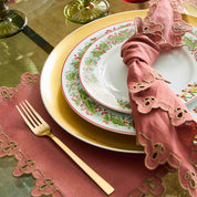 Decorative table setting with gold cutlery, red napkin, and patterned plates on a reflective surface.