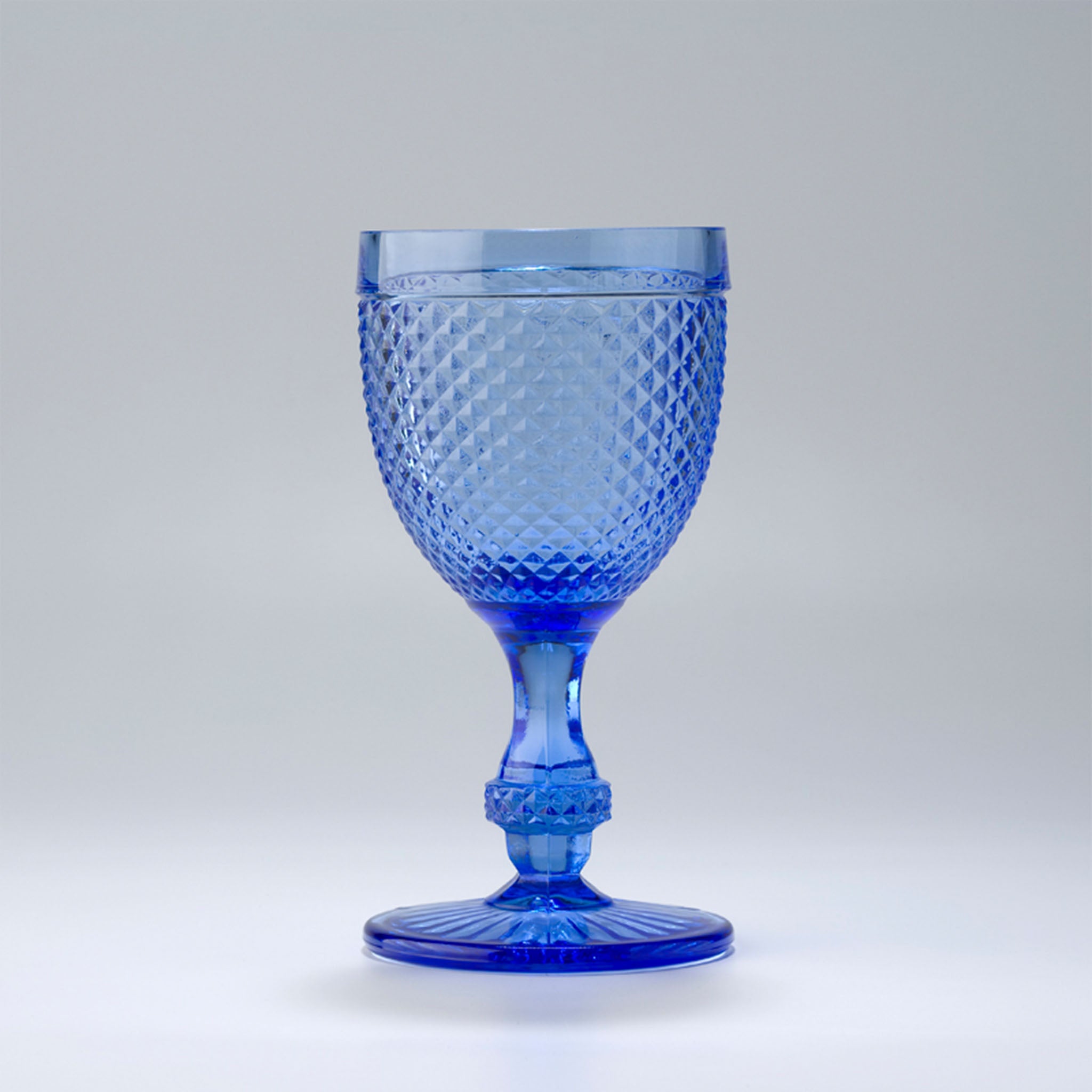 An blue-colored wine glass with a geometric pattern and a stem, against a white background.
