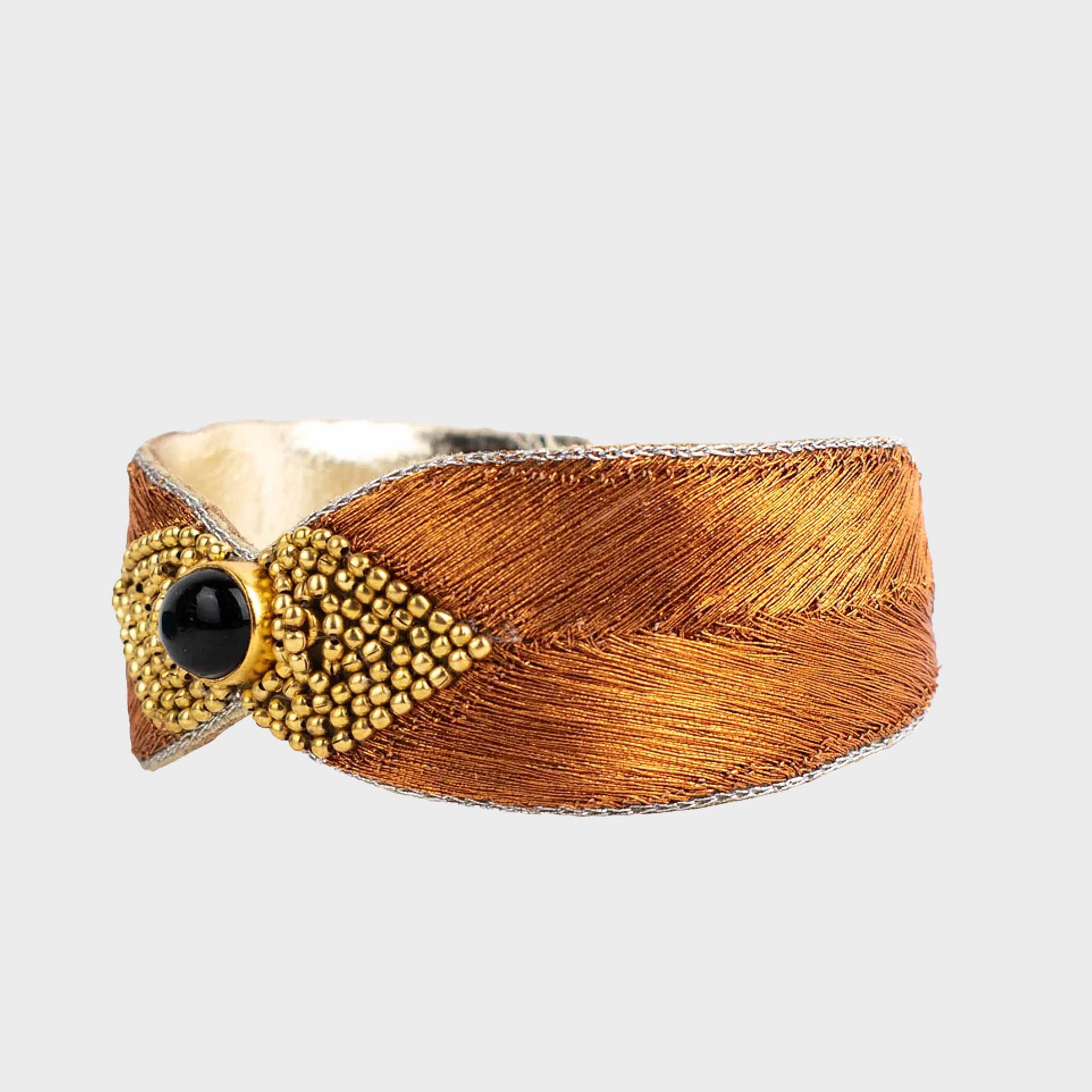 Bracelet with amber embroidered strap, gold accents, and black bead on a light gray background