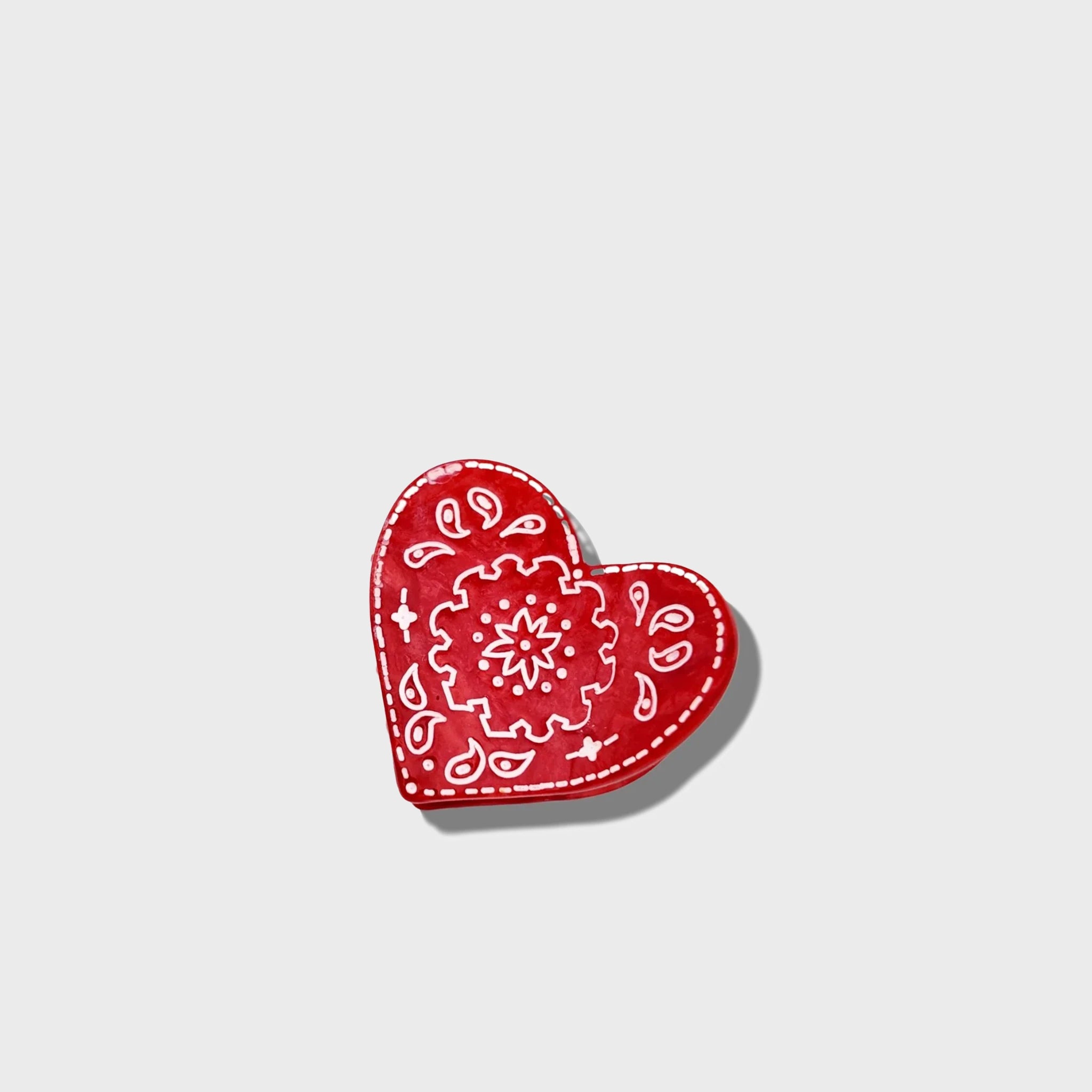 Red heart-shaped decorative item with white patterns on a light gray background