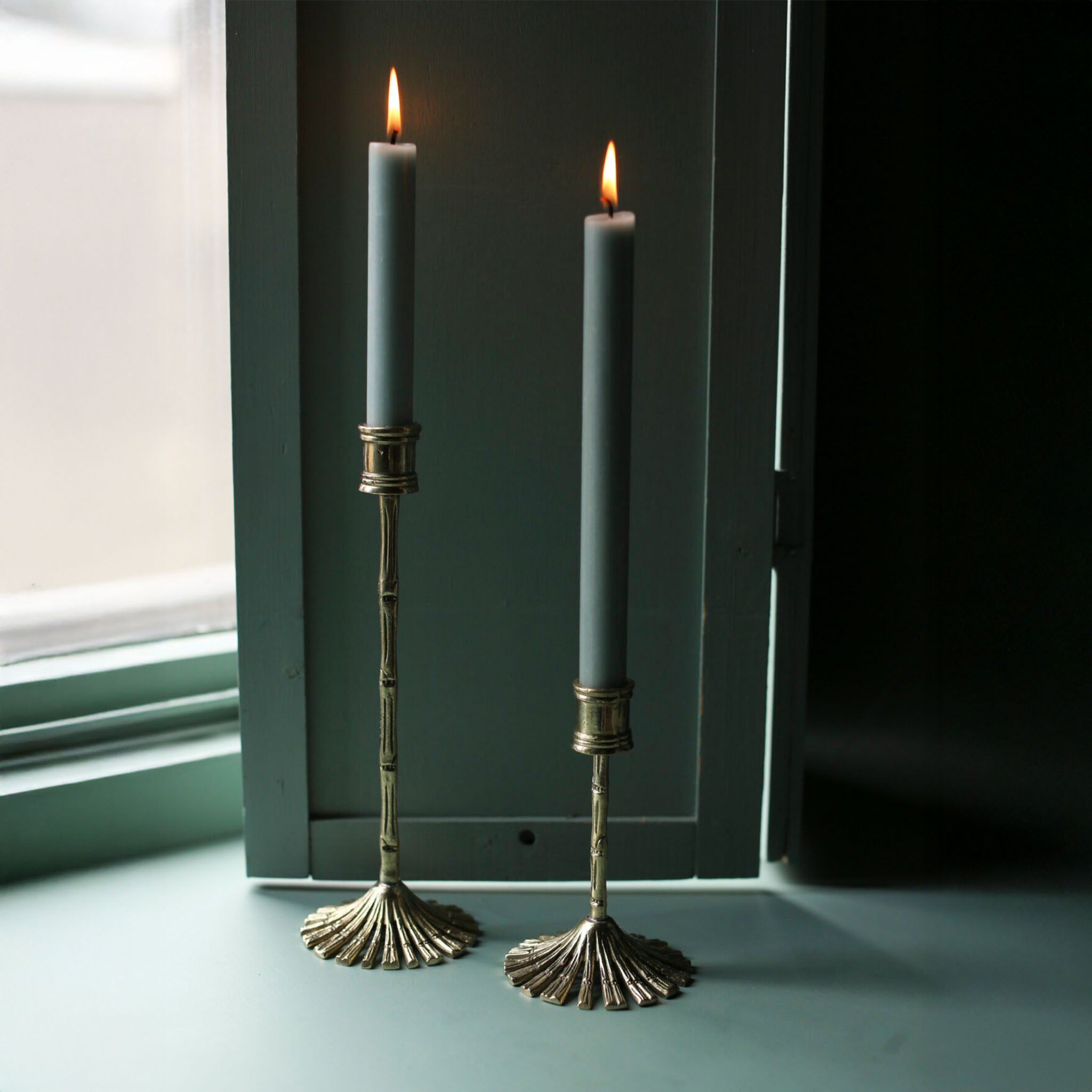 Brass bamboo candle holders with green taper candles by a window