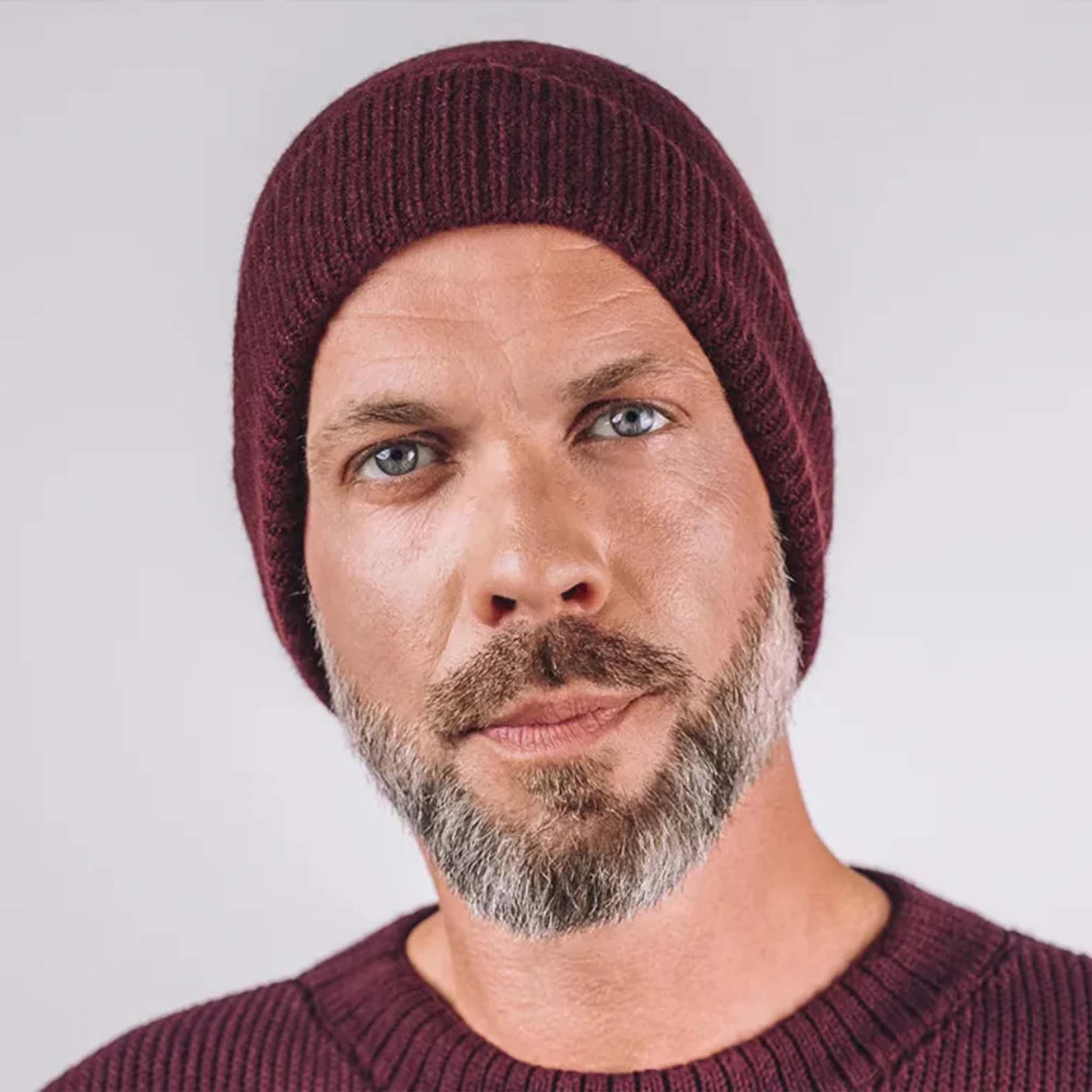 Man wearing a maroon knit beanie and sweater against a plain background
