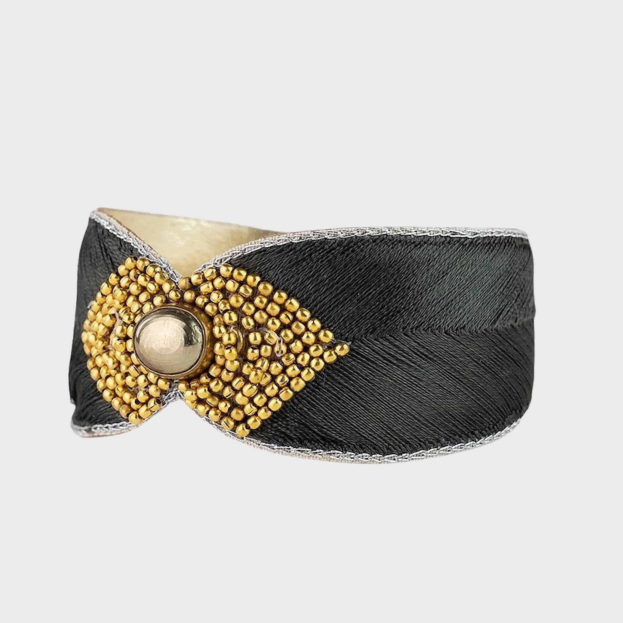 Black bracelet with gold decorative element on a light gray background
