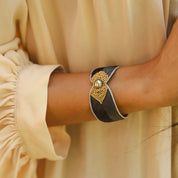 Close-up of a wrist wearing a decorative bracelet with a pearl and gold accents, against a beige background.