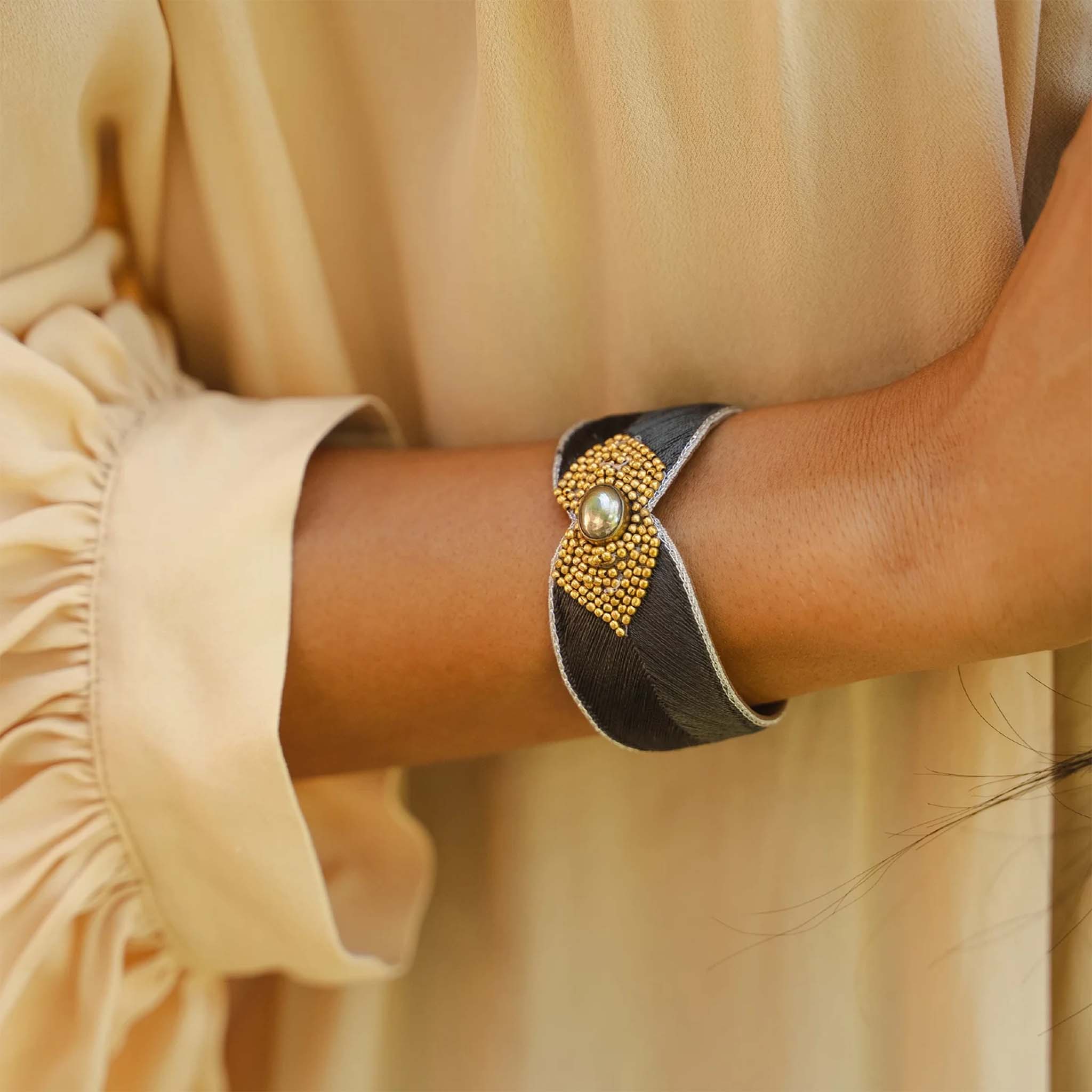 Close-up of a wrist wearing a decorative bracelet with a pearl and gold accents, against a beige background.