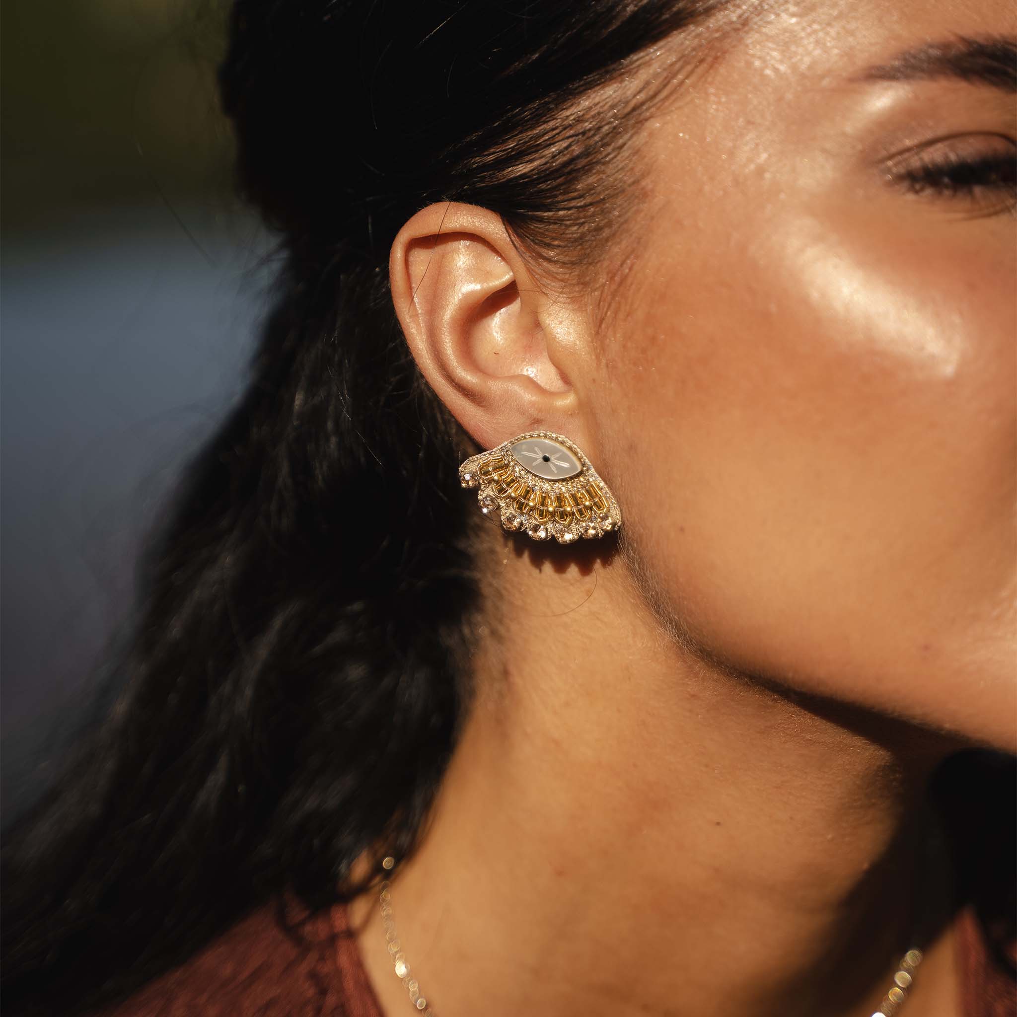 Close-up of a woman wearing a gold and diamond earring with a blurred background