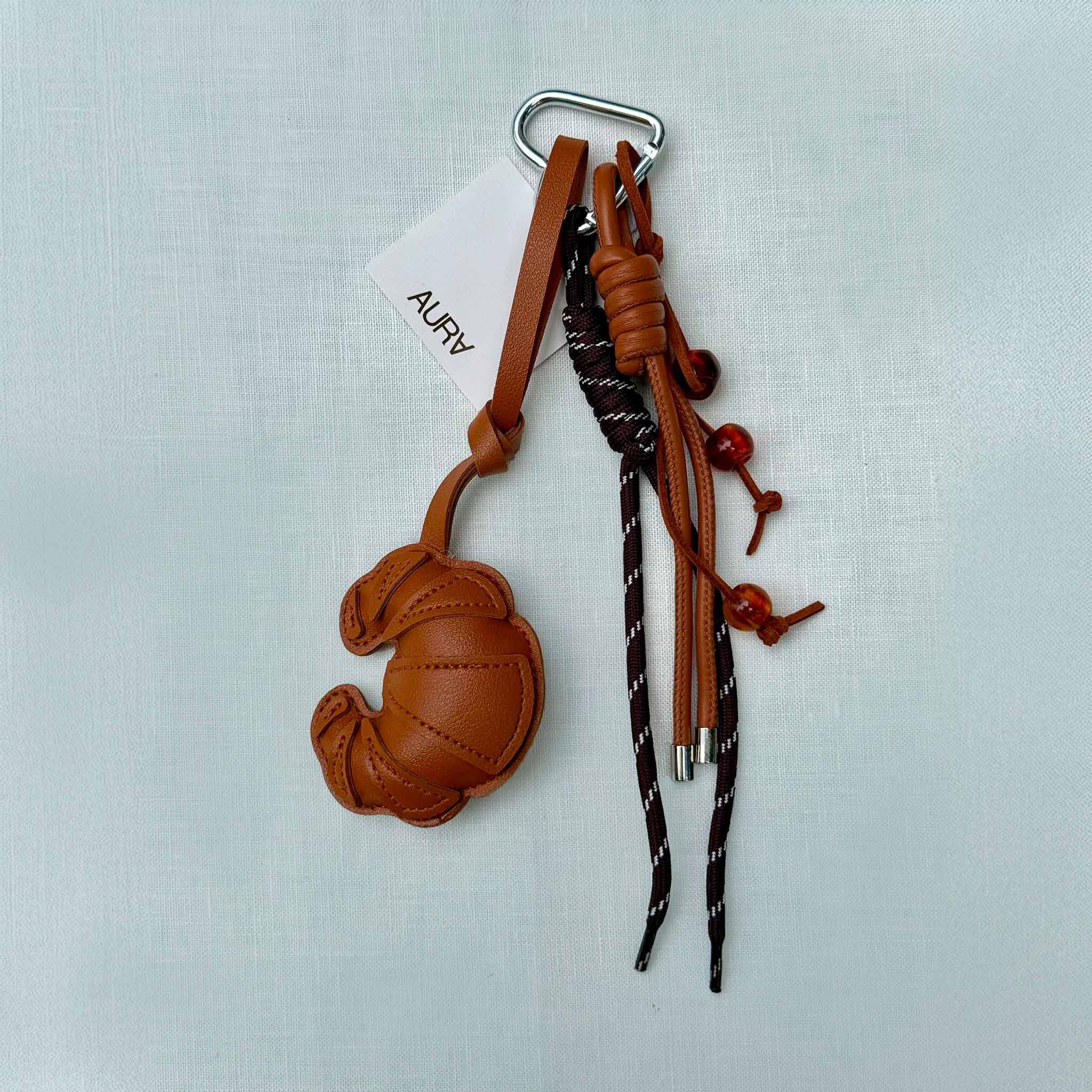 Croissant Bag Charm in brown leather with braided rope cords and metal clip