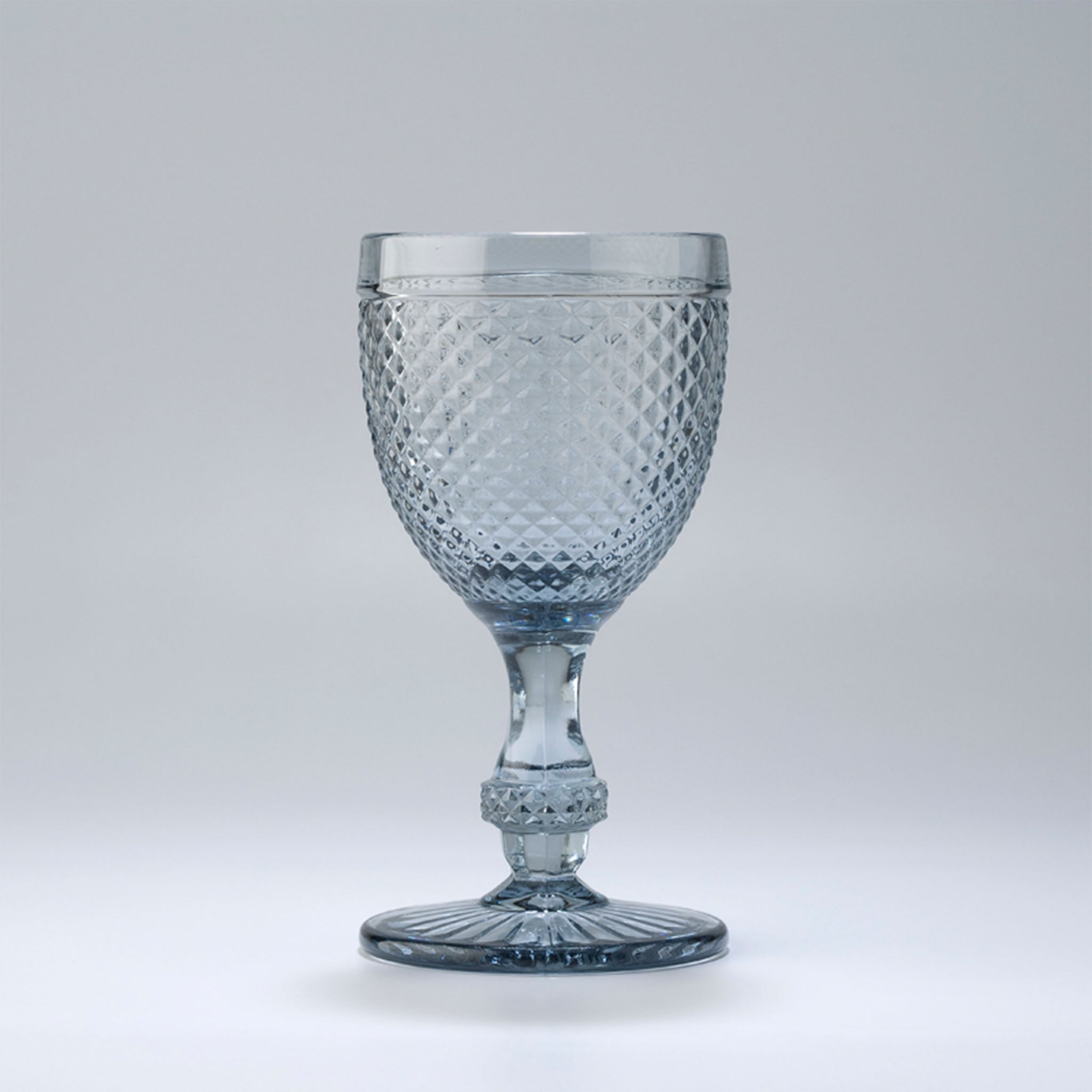 An clear-colored wine glass with a geometric pattern and a stem, against a white background.
