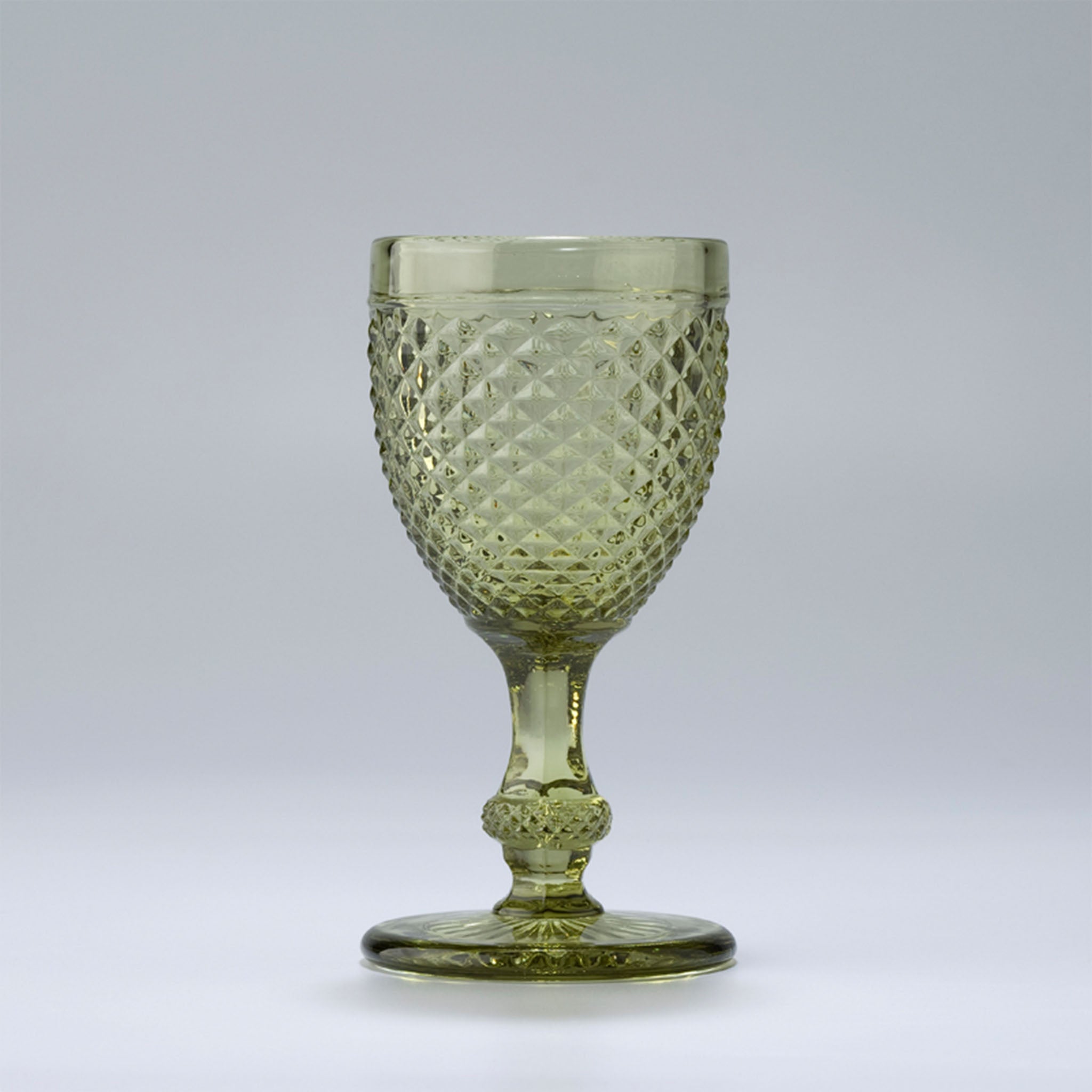 An light green-colored wine glass with a geometric pattern and a stem, against a white background.