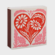Foto de producto de la caja de fósforos Heart Box de Aura Collective: corazón rojo con detalle floral en rosa y blanco sobre fondo crema.