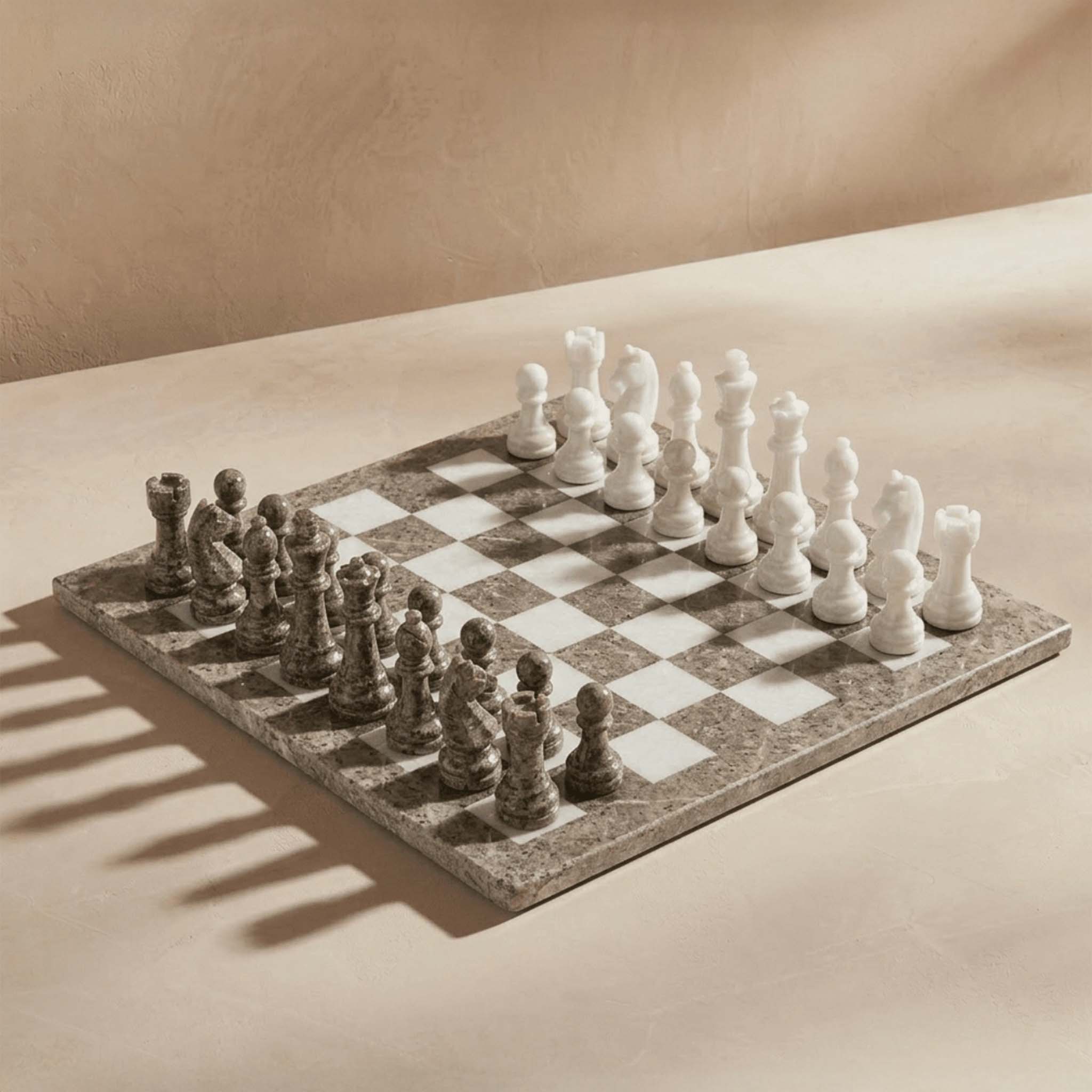 A marble chess set with a checkered board, featuring white and gray stone pieces arranged on a beige surface with soft shadows.