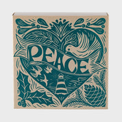 Foto de producto de la caja de fósforos Peace Matches de Aura Collective: diseño en verde azulado sobre fondo kraft con un corazón formado por una paloma, la palabra Peace y un faro, rodeado de ramas de acebo y pino.