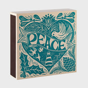 Vista frontal de la caja de fósforos Peace Matches de Aura Collective, con el mismo diseño de paloma, faro y motivos navideños en verde azulado sobre fondo kraft.