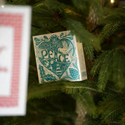 Caja de fósforos Peace Matches de Aura Collective colgada entre las ramas de un árbol de Navidad iluminado.