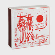 Foto de producto de la caja de fósforos Perfect Match Cowboy Couple de Aura Collective: ilustración en rojo de una pareja de vaqueros bajo el sol, con el texto Perfect Match, Love Love Love y una calavera de toro, de la colección Saint No.