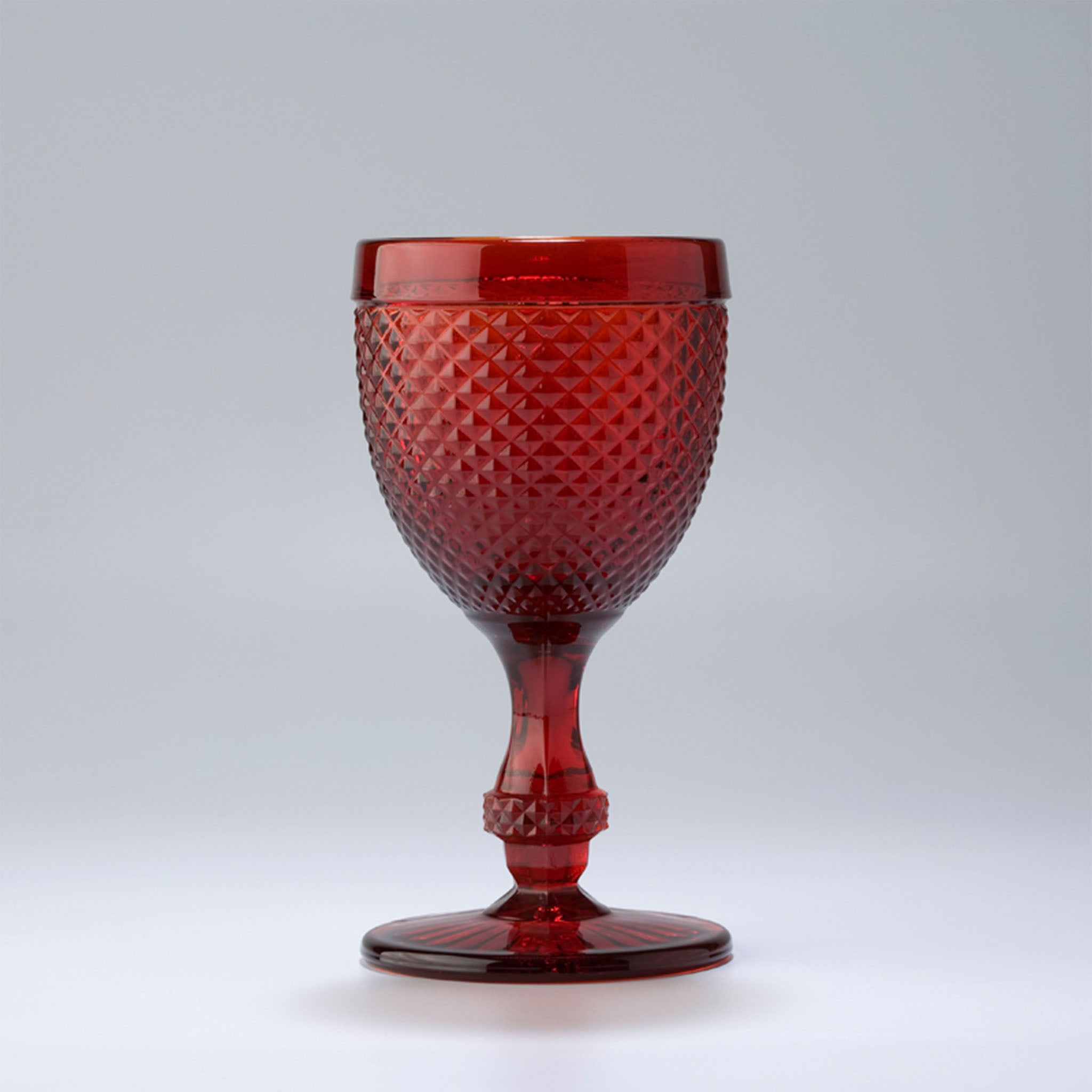 An red-colored wine glass with a geometric pattern and a stem, against a white background.