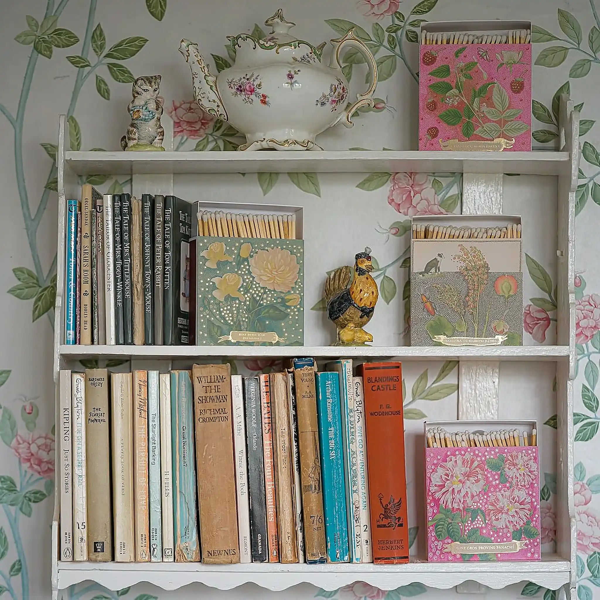 Caja de fósforos Rose Provin Petunia de Aura Collective en una repisa junto a libros y otras cajas de fósforos florales de la misma colección, con una tetera de porcelana de fondo.