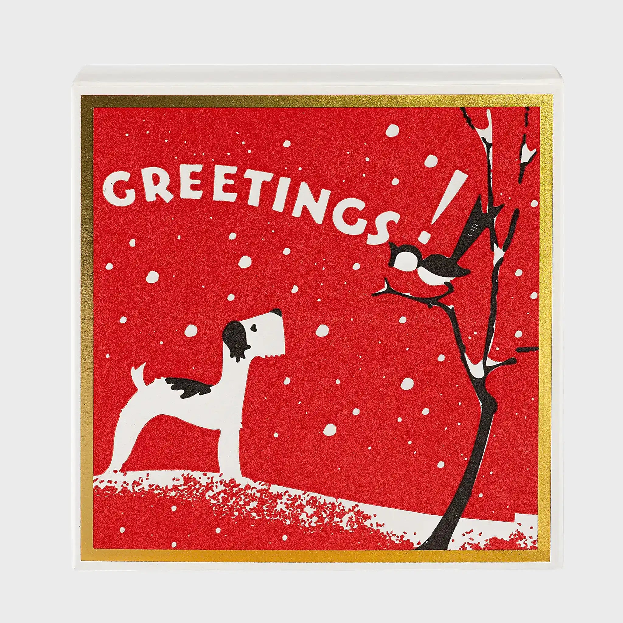 Foto de producto de la caja de fósforos Season's Greetings de Aura Collective: fondo rojo con marco dorado, un perro terrier mirando un pájaro sobre un árbol nevado y el texto Greetings!.