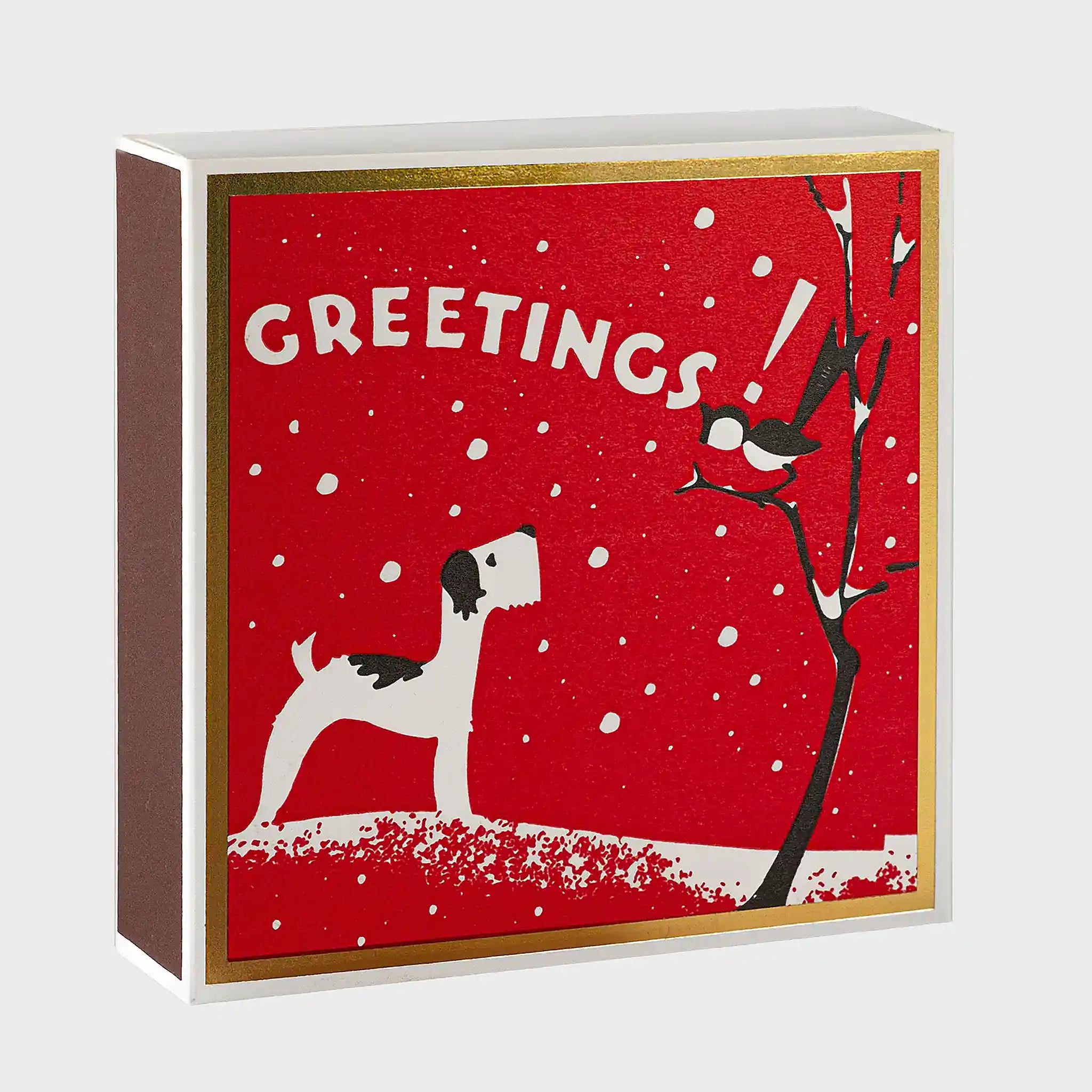 Vista en ángulo de la caja de fósforos Season's Greetings de Aura Collective, mostrando el grosor de la caja con el mismo diseño de perro, pájaro y árbol nevado sobre fondo rojo.