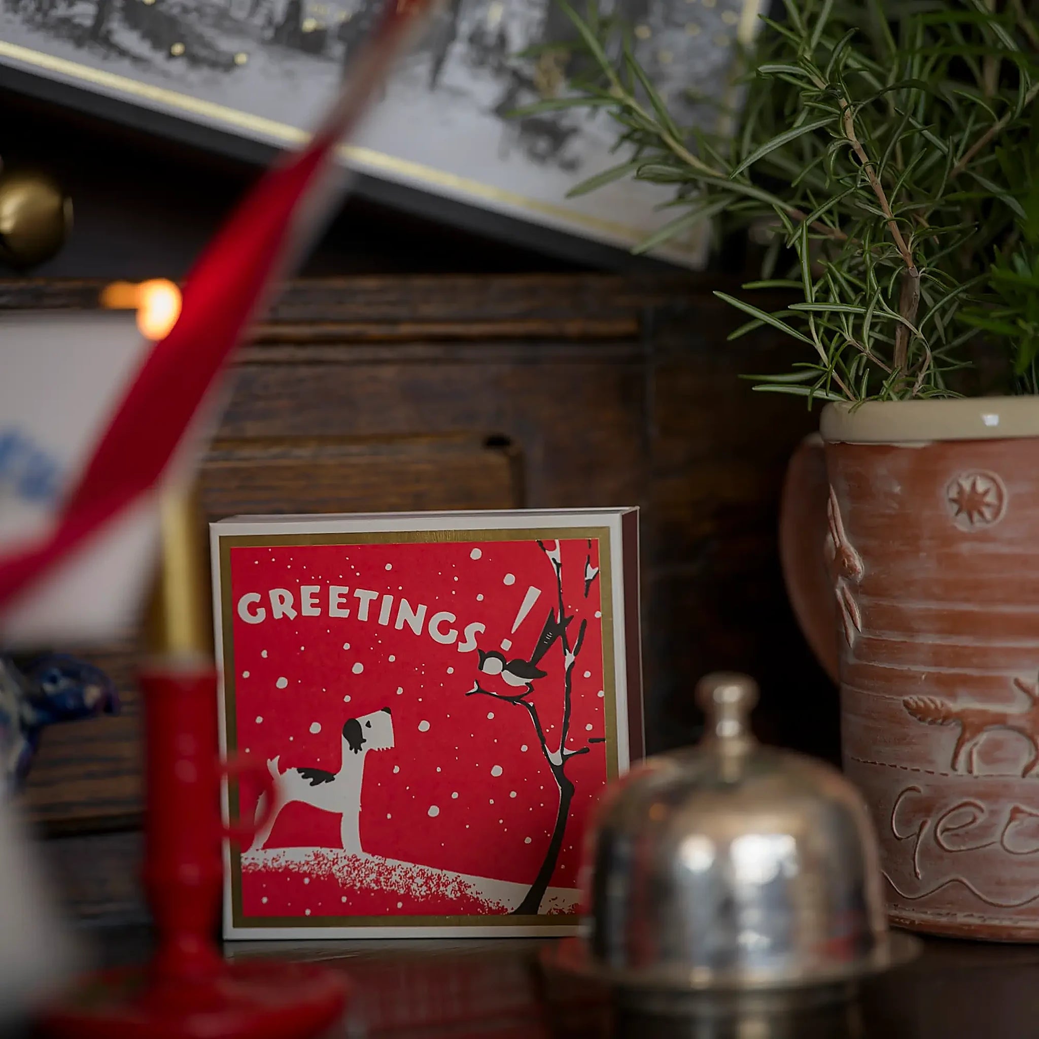 Caja de fósforos Season's Greetings de Aura Collective en una escena navideña, junto a velas encendidas y una planta de romero.