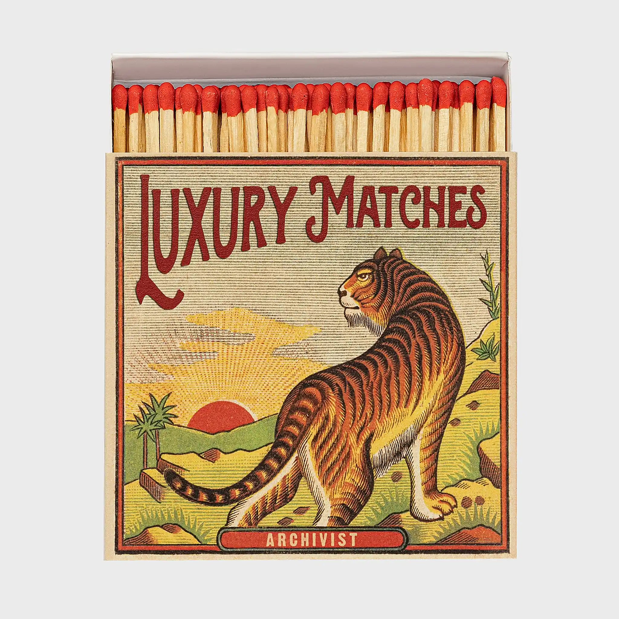 Foto de producto de la caja de fósforos Sunrise Tiger de Aura Collective: ilustración vintage de un tigre frente a un atardecer con palmeras, con el texto Luxury Matches y Archivist.