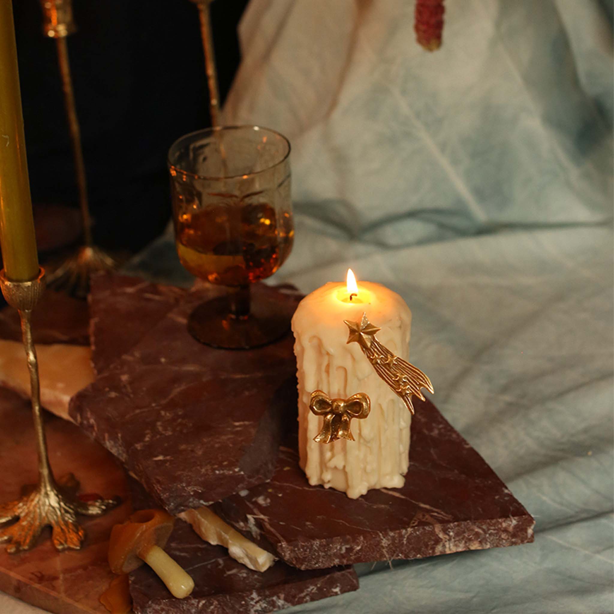 Brass shooting star candle pin on a lit white pillar candle with amber glassware