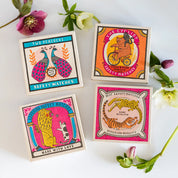 Caja de fósforos Two Peacocks de Aura Collective junto a otras cajas de fósforos de diseño con animales (un oso ciclista, un león y un gato, un leopardo y un tigre) y flores.