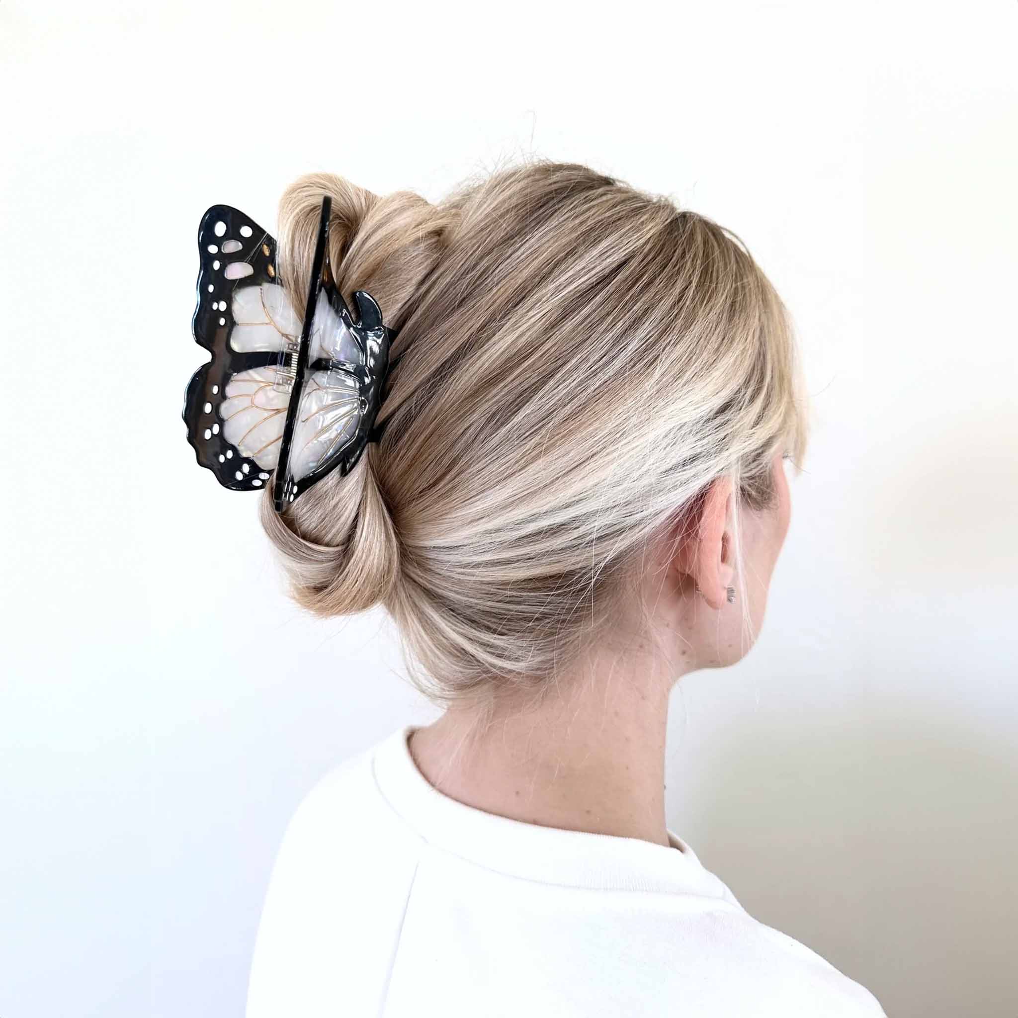 A person with their back turned to the camera has their hair styled in a bun, secured with a large black and white butterfly hair clip.
